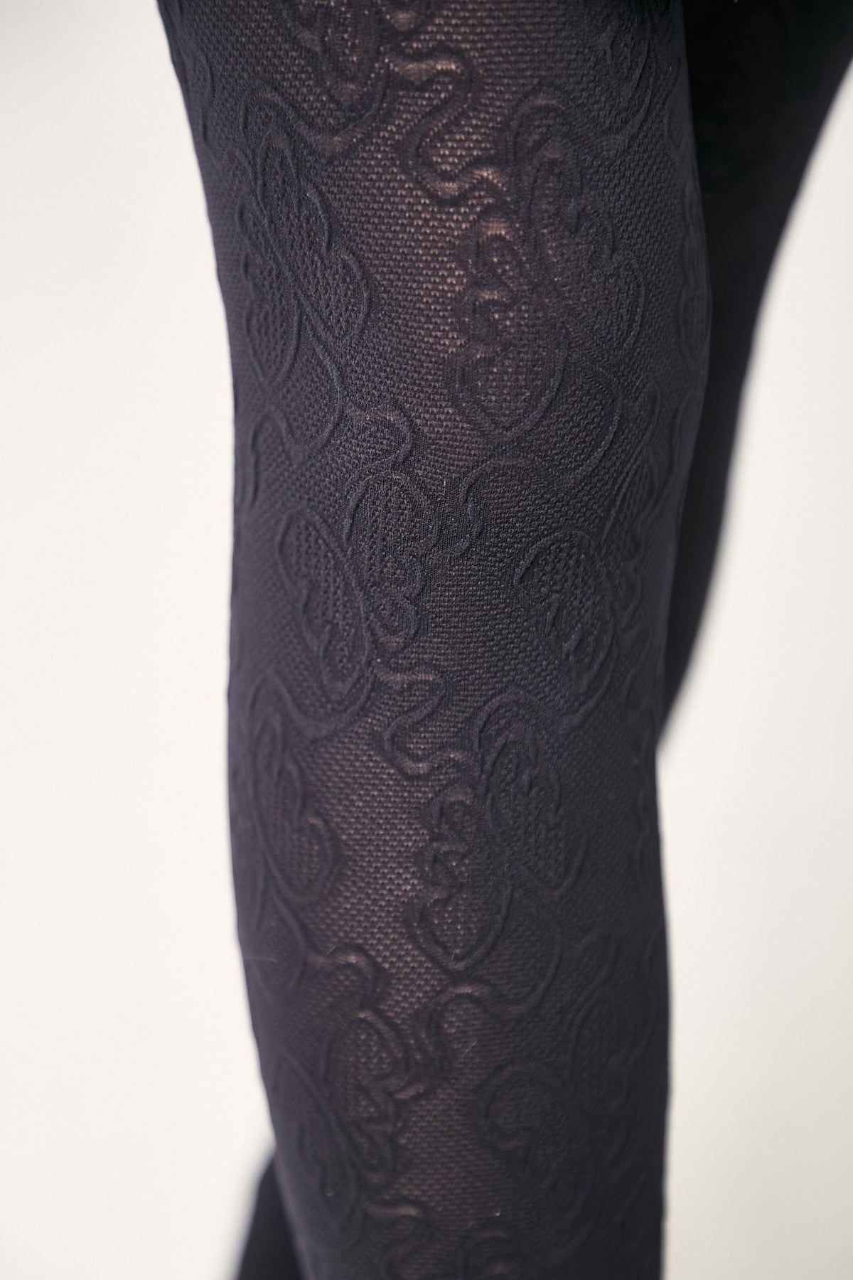 Black tights with a textured floral pattern covering the fabric against a plain white background.