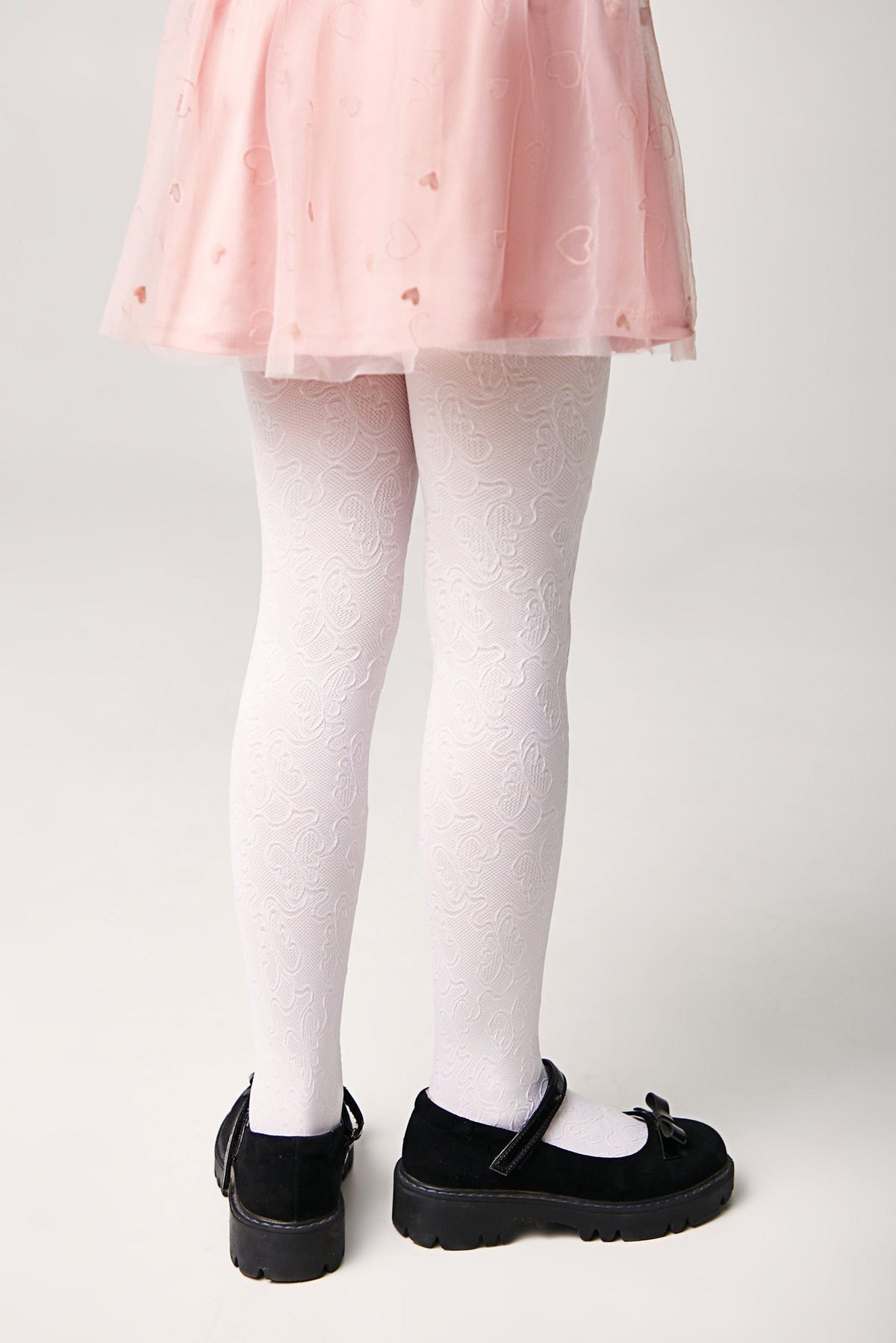 White tights with a subtle embossed floral pattern are worn with a light pink heart-patterned skirt and black mary jane shoes with thick soles.