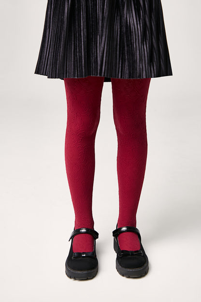 A pair of red patterned tights worn with a black pleated skirt and black Mary Jane shoes featuring a bow detail.