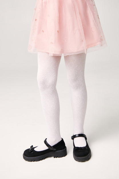 A child wears white patterned tights with a light pink tutu skirt and black Mary Jane shoes.