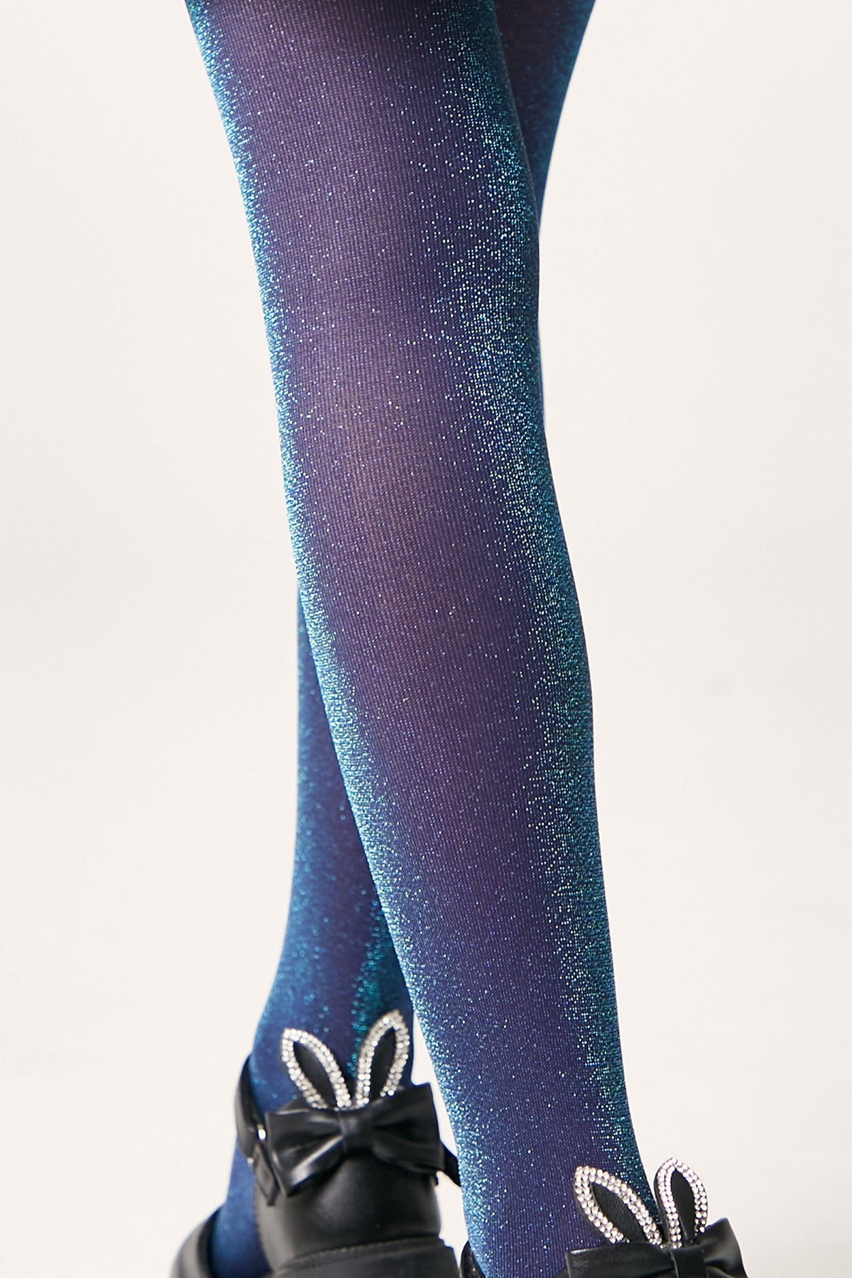 Shimmering deep blue and turquoise gradient tights worn with black Mary Jane shoes featuring rhinestone-embellished rabbit ears on the straps.