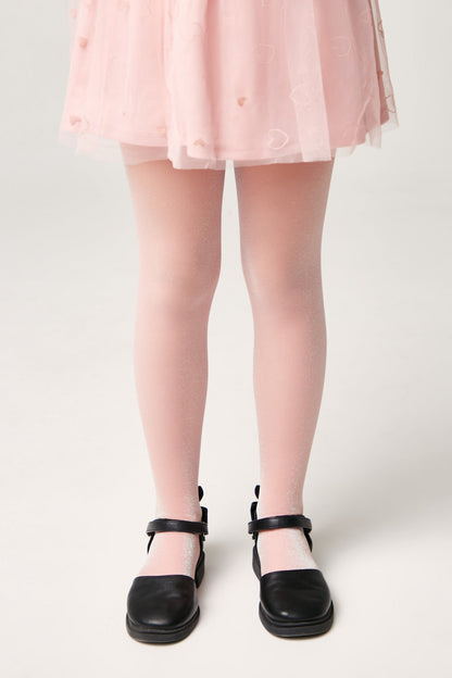 A child wears shimmering light pink tights paired with black Mary Jane shoes and a pale pink heart-patterned tulle skirt.