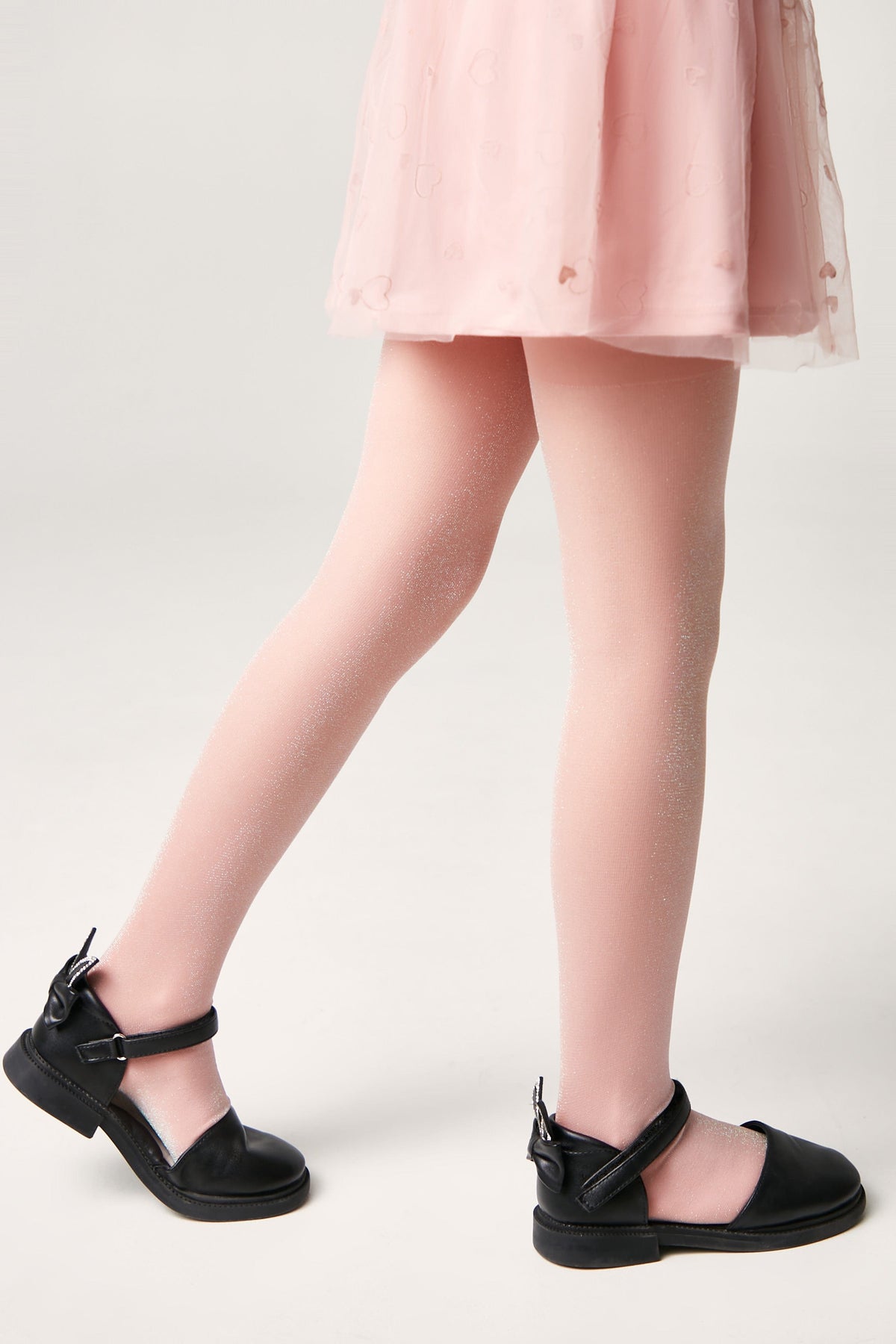 Light pink glittery tights worn by a child wearing a light pink skirt and black buckled sandals.