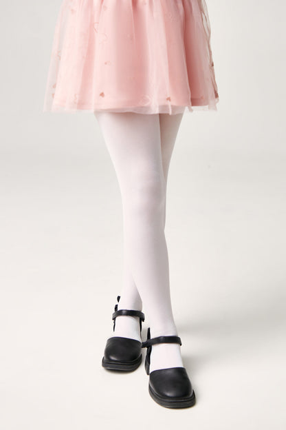 A pair of opaque white tights worn with a pink tulle skirt and black Mary Jane shoes against a white background.