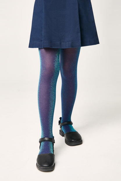 Ombre tights transition from a deep navy blue at the top to a bright teal blue at the feet, featuring an all-over subtle glitter finish and worn under a dark skirt with black buckled shoes.