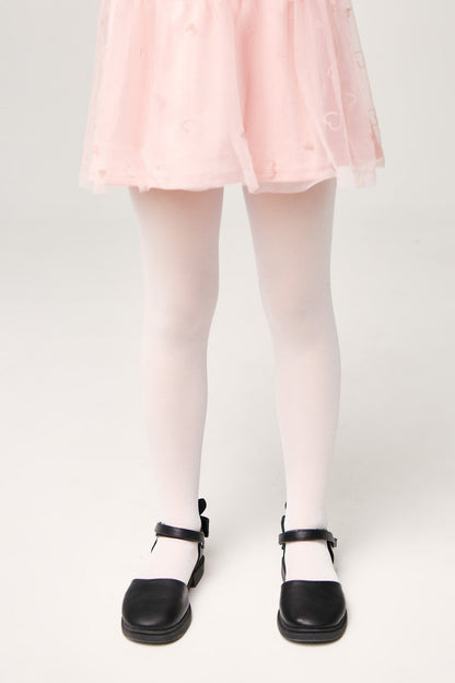 A pair of opaque white tights worn with a pink skirt featuring a subtle heart pattern and black flat buckled shoes.