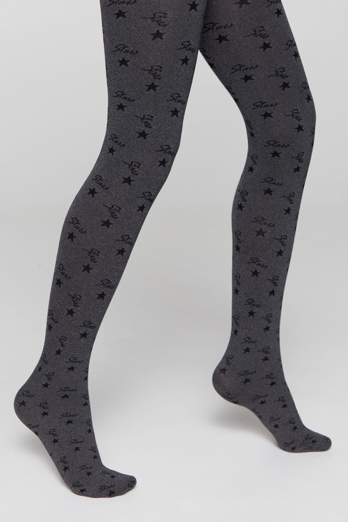 A pair of grey tights featuring a repeating pattern of black stars and the cursive word Stars against a light grey background, shown on legs against a neutral backdrop.
