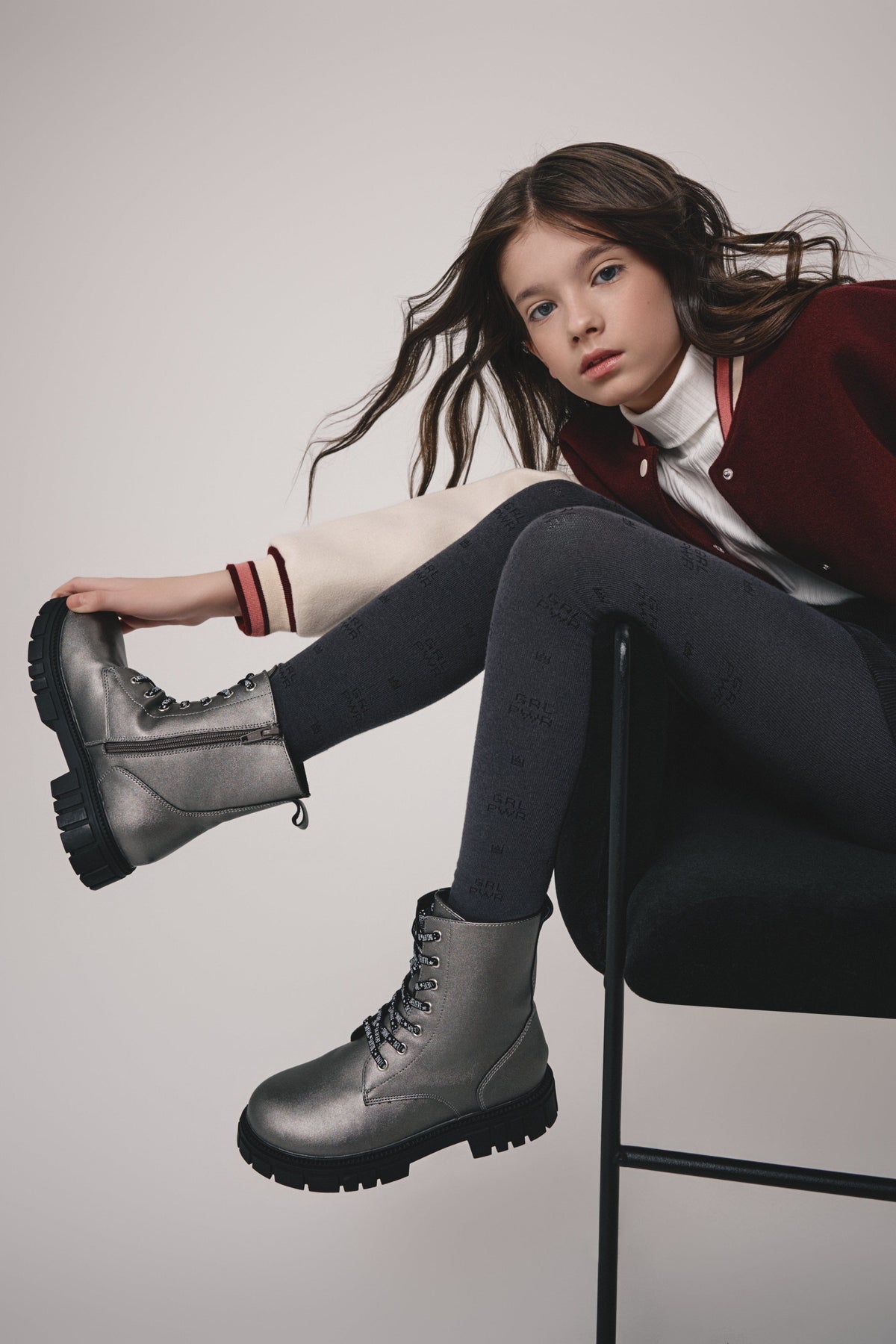 Metallic silver ankle boots with black chunky lug soles, laces, and side zippers worn by a young girl sitting on a chair.