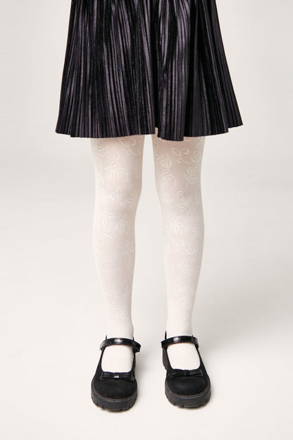 A child wears white tights with a subtle leaf pattern paired with a black pleated skirt and black Mary Jane shoes.