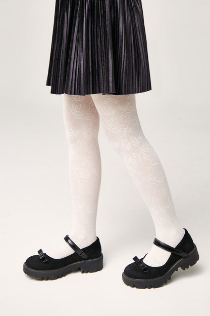 White tights with a delicate leaf pattern are worn with a black pleated skirt and black platform Mary Jane shoes against a solid light background.