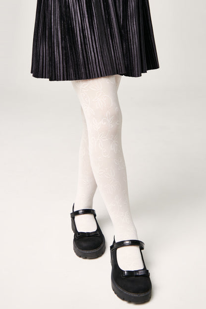 White patterned tights with a delicate leaf design worn with a black pleated skirt and black Mary Jane shoes featuring small bows.