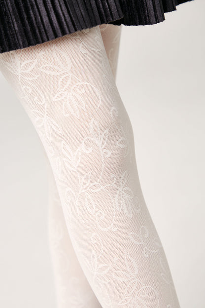 White patterned tights with a delicate leafy floral design worn under a black pleated skirt against a plain background.