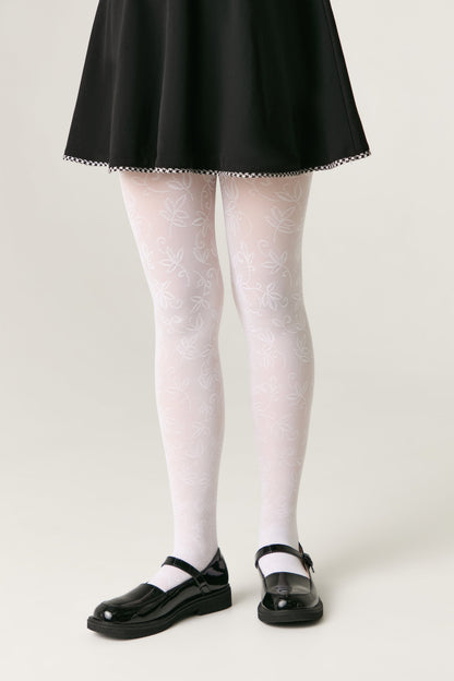 A pair of white tights featuring a delicate, subtle leafy vine pattern, worn with a black skirt and glossy black Mary Jane shoes against a plain grey background.