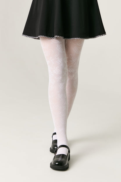 White patterned tights featuring delicate line-drawn leaf designs worn with a black flared skirt and black Mary Jane shoes.