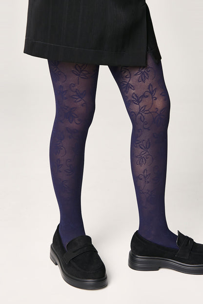 A pair of deep blue patterned tights featuring a delicate floral vine design, worn under a black skirt with black platform loafers.