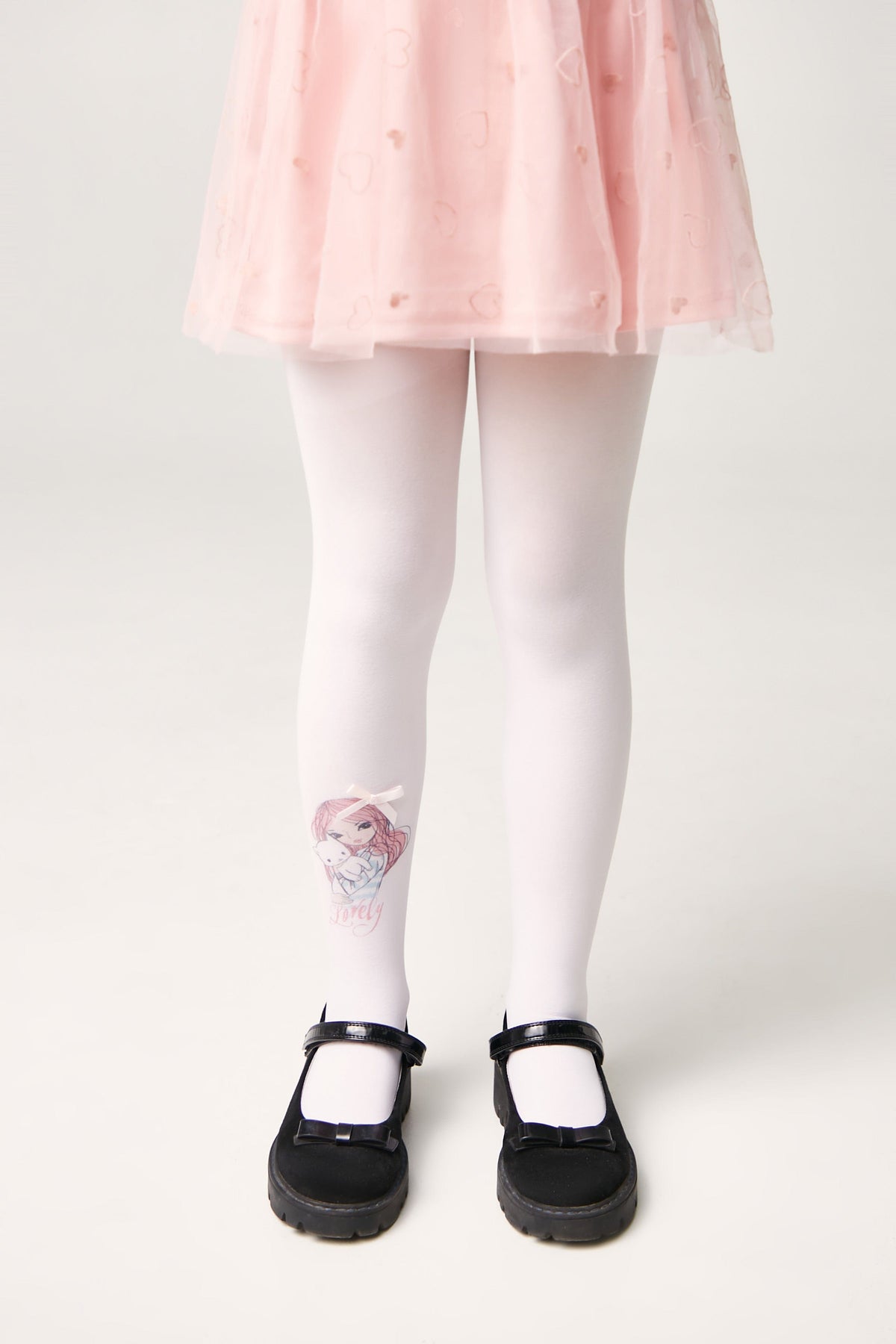 A pair of opaque white tights featuring a cartoon girl illustration on the left lower leg, worn by a child with a light pink tulle skirt and black mary jane shoes against a plain white background.