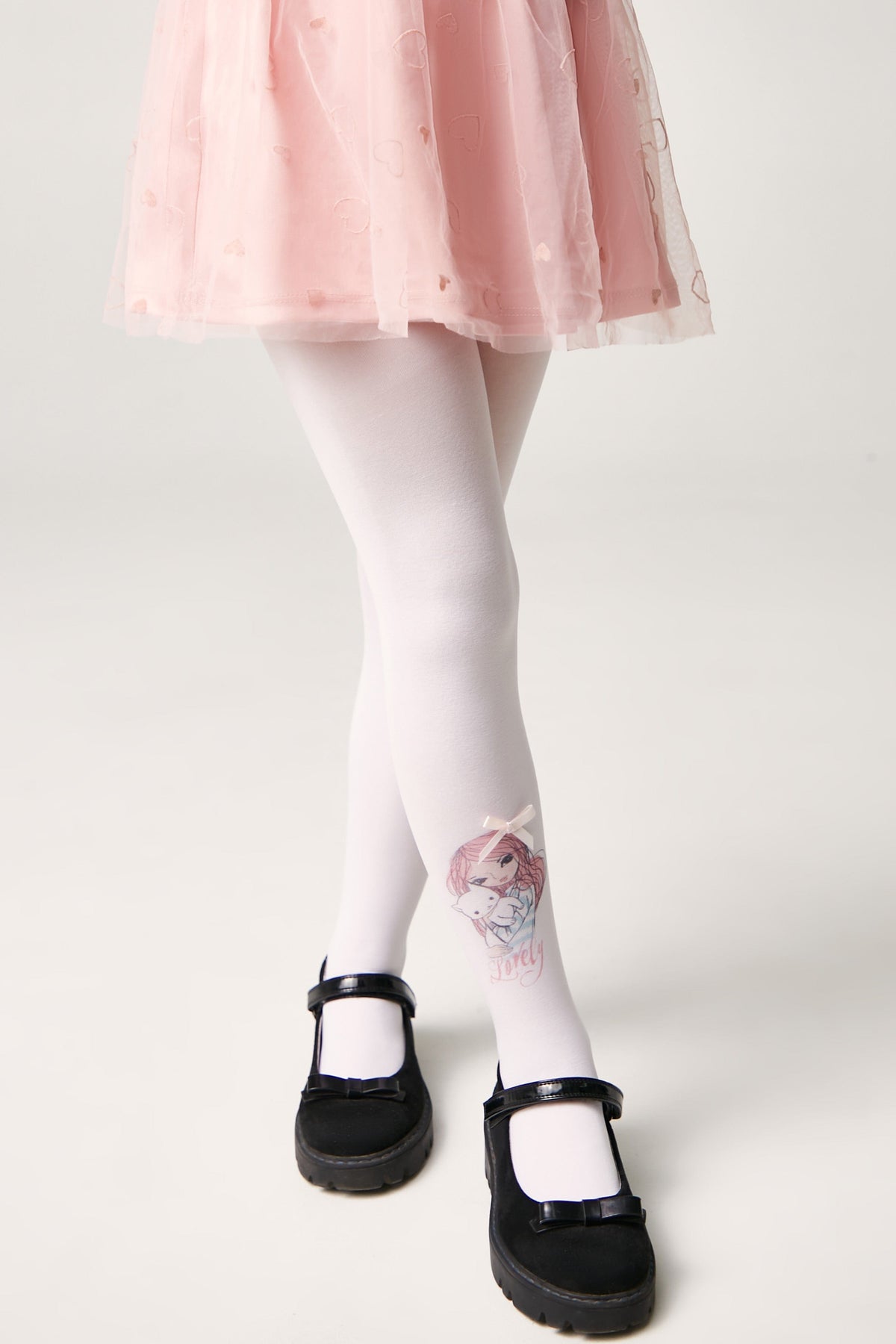 White tights with a cartoon girl graphic on the left leg, worn with a pink pleated skirt and black Mary Jane shoes.