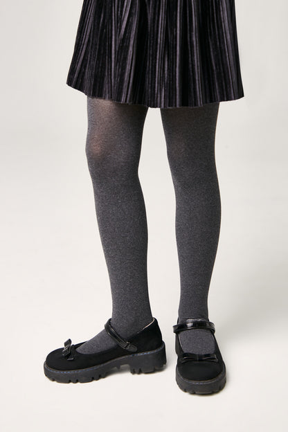 A person wears a dark grey pleated skirt with matching grey tights and black flat shoes featuring a decorative bow and an adjustable strap.