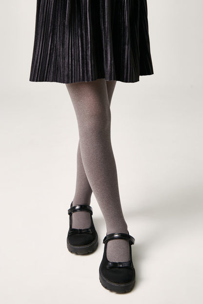 A person wears a black pleated skirt with opaque grey tights and black mary jane shoes with a strap and small bow detail.