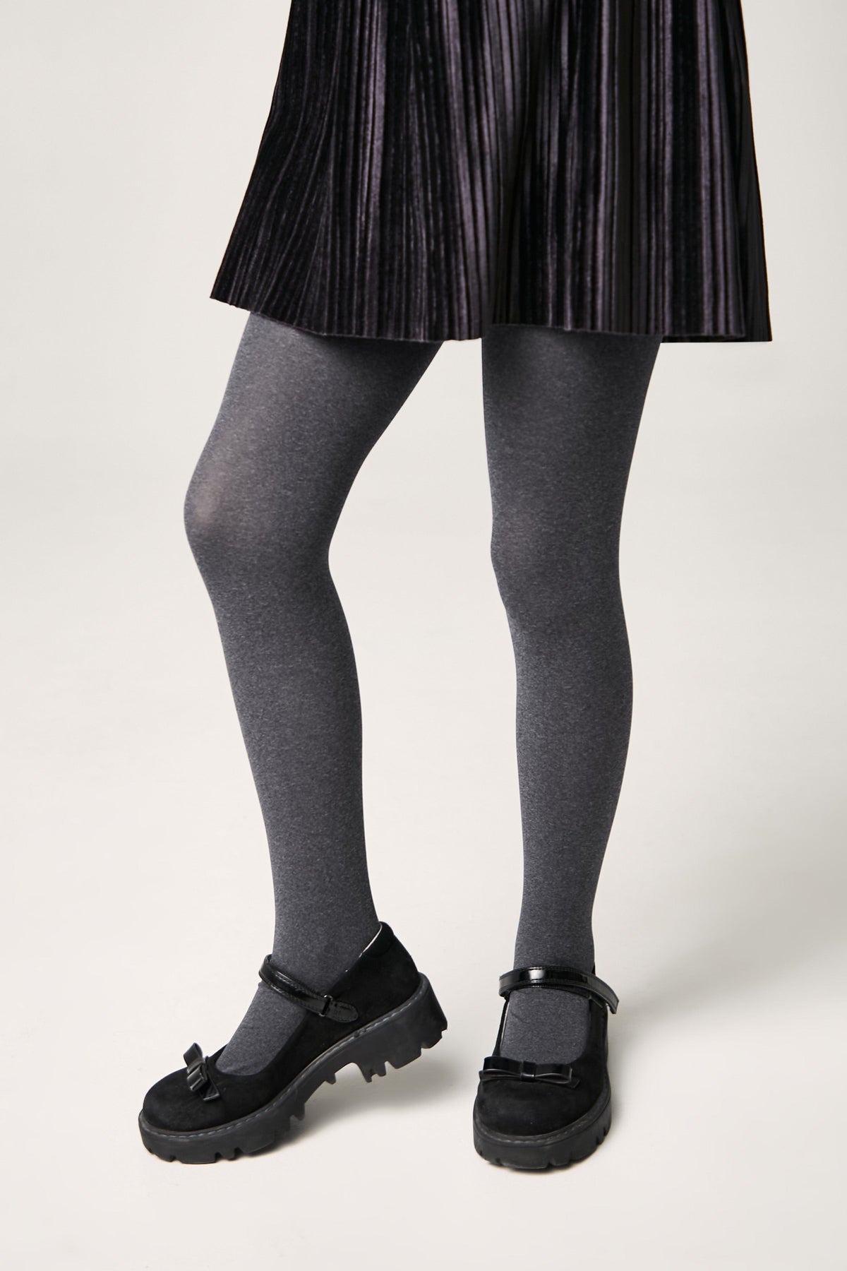 A pair of charcoal grey tights worn with a black pleated skirt and black Mary Jane shoes with thick rubber lug soles.