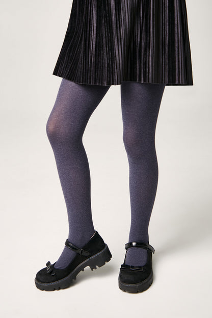 A person wears a black pleated skirt, grey tights, and black Mary Jane shoes with bow accents on a neutral background.