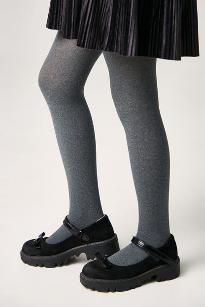 A person wearing a pleated black skirt, grey tights, and black Mary Jane shoes with thick lug soles.