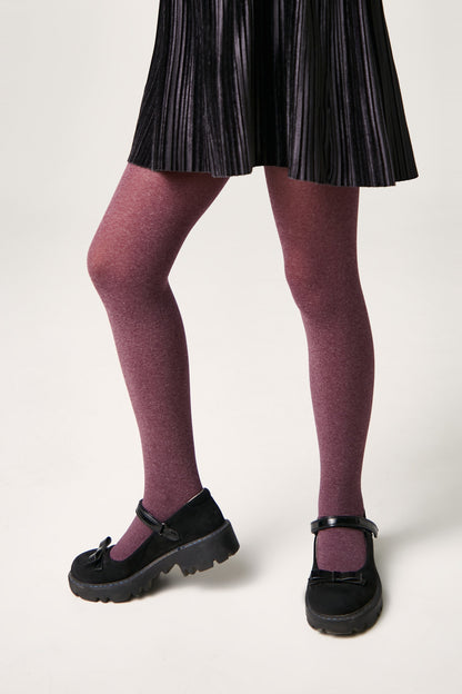 A person wears a black pleated skirt with opaque maroon tights and black Mary Jane shoes featuring a bow detail and chunky soles.