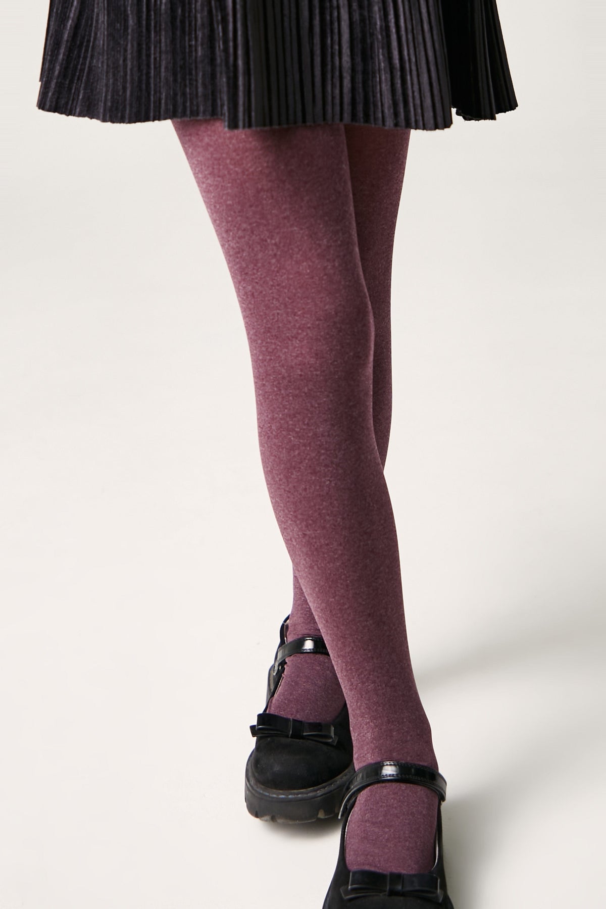 Burgundy opaque tights paired with a black pleated skirt and black Mary Jane shoes.
