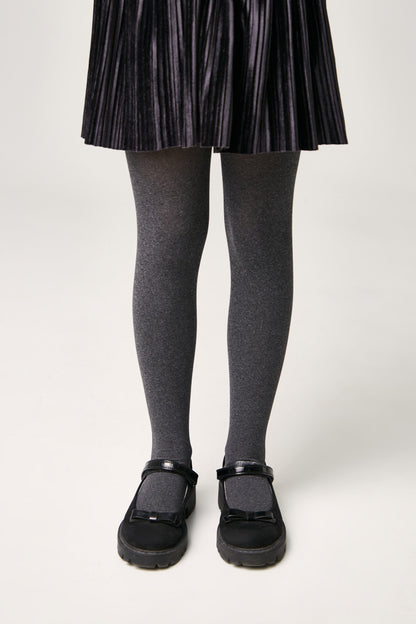 A pair of opaque grey tights worn with black Mary Jane style shoes featuring a bow detail on a plain white background.