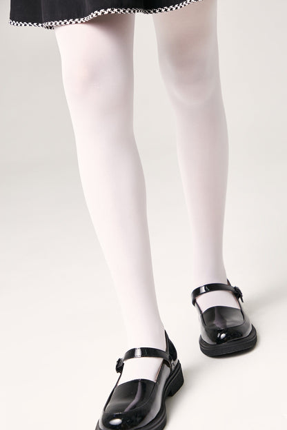 A pair of shiny black patent leather Mary Jane shoes worn with opaque white tights and a black skirt.