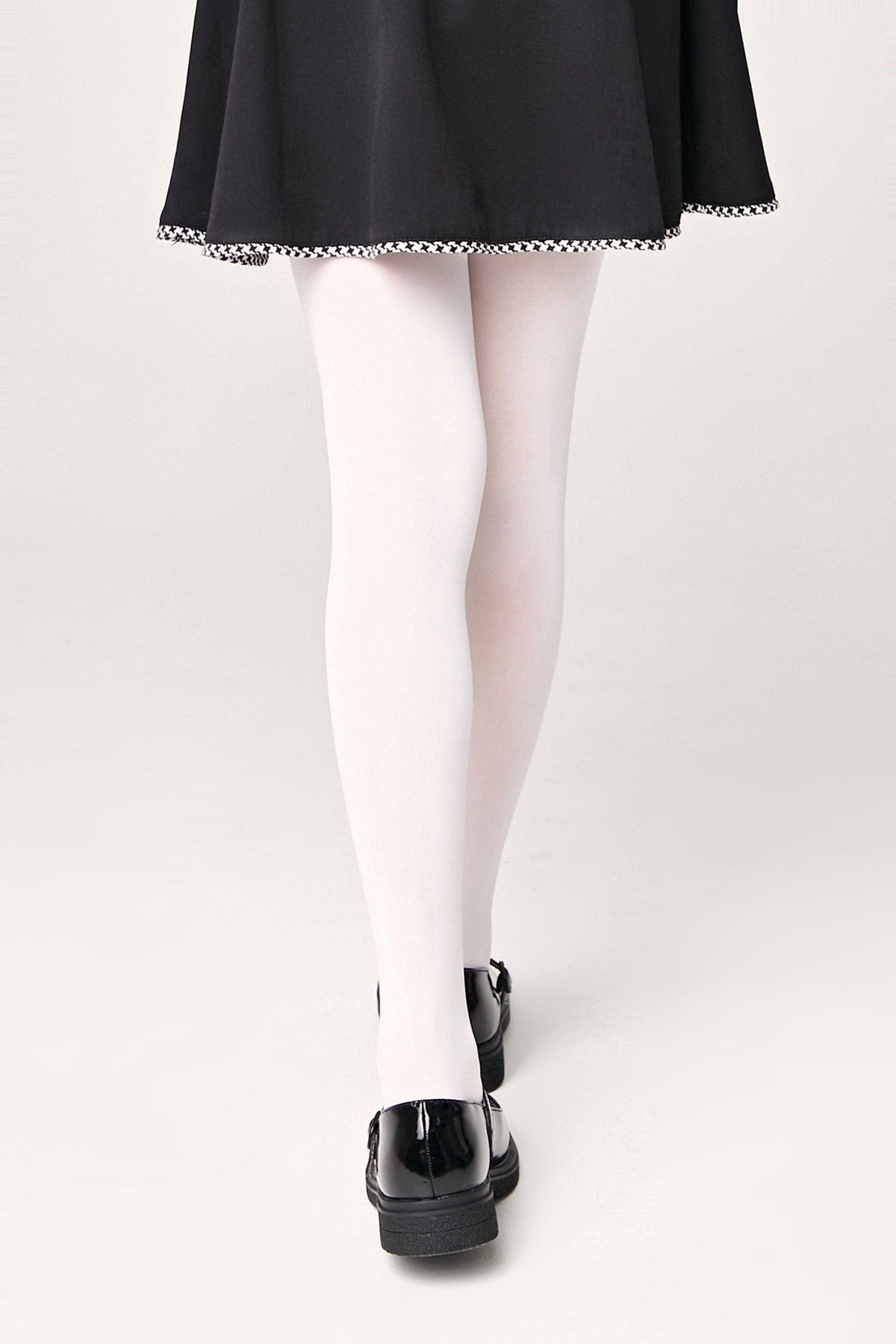 A person wears white opaque tights and black glossy shoes with a black skirt featuring a houndstooth trim.