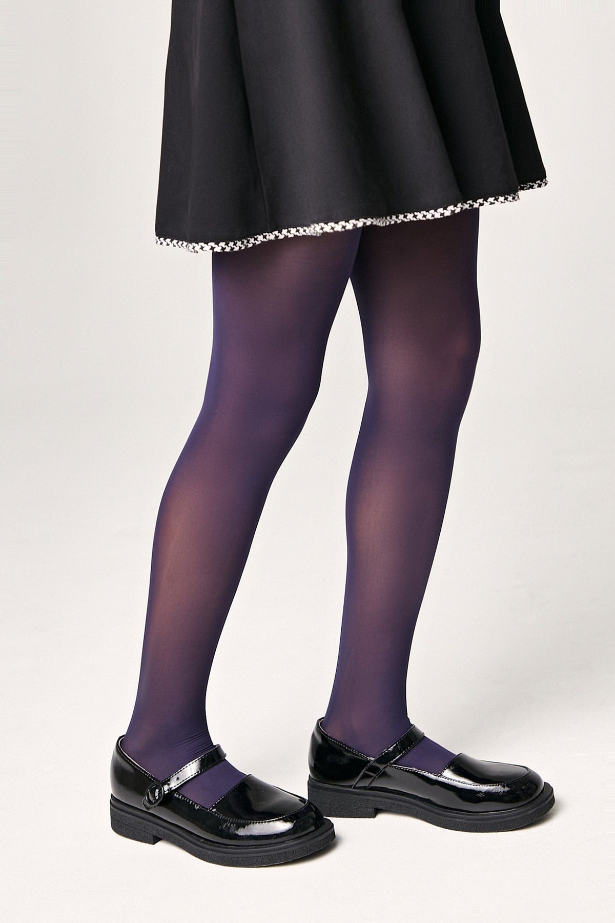 A person wears purple tights with black Mary Jane shoes and a black skirt with a white patterned trim.
