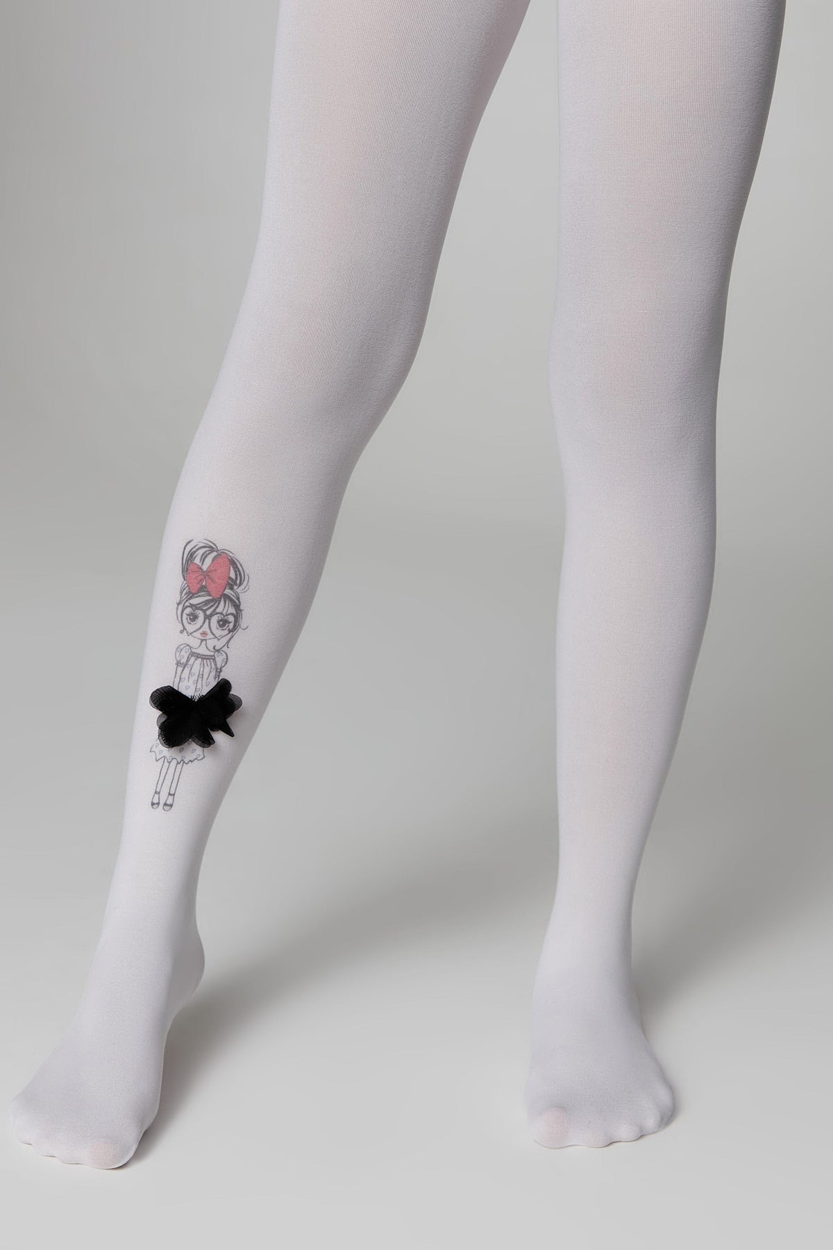 White opaque tights are worn on a pair of legs, featuring a whimsical black and white illustrated girl graphic with a black fabric bow embellishment on the outer side of the right calf.