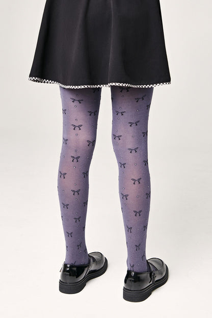 A person wears purple tights patterned with small dark bows and subtle sparkles, paired with a black skirt and black Mary Jane flats.