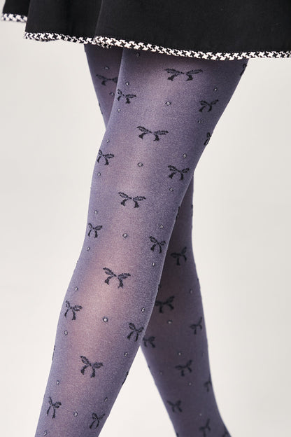 Blue-grey patterned tights featuring a repeating motif of small dark bows and tiny shimmering dots on a person wearing a black skirt.