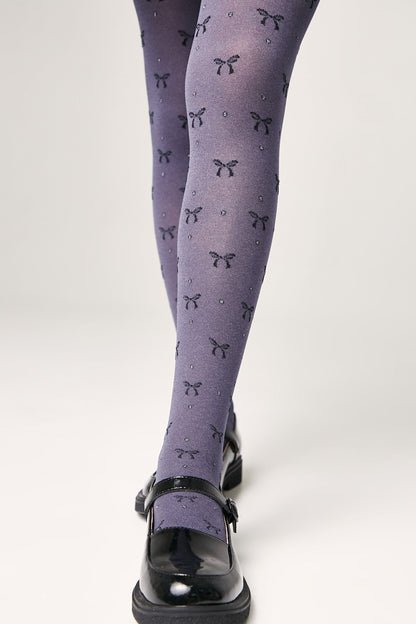 Grey tights featuring a repeating pattern of small dark bows and subtle glitter accents are worn with black patent leather Mary Jane shoes.