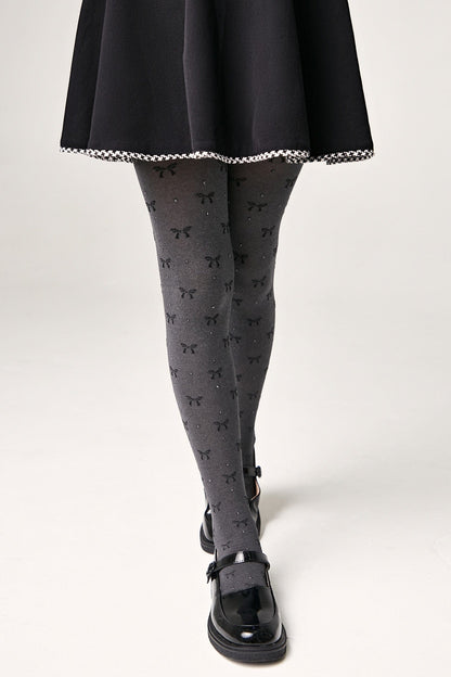 Grey tights patterned with small black bows and subtle glitter accents are worn with a black skirt and black buckled flat shoes.