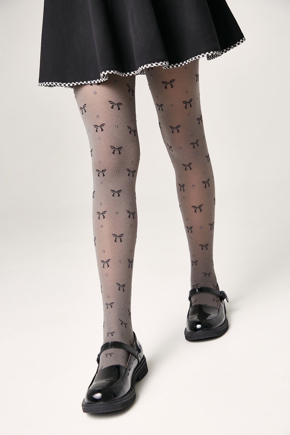 Sheer grey tights featuring a recurring pattern of small black bows and tiny sparkling rhinestones, worn with a black skirt and shiny black Mary Jane flats.