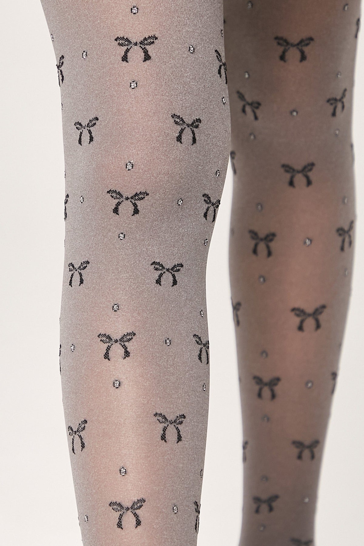 Sheer grey tights patterned with repeating small black bows and tiny silver glitter dots worn on legs.