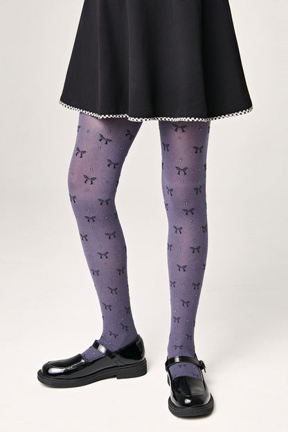 Grayish-purple tights patterned with small black bows and tiny rhinestones worn with a black skater skirt and black patent leather mary jane shoes.