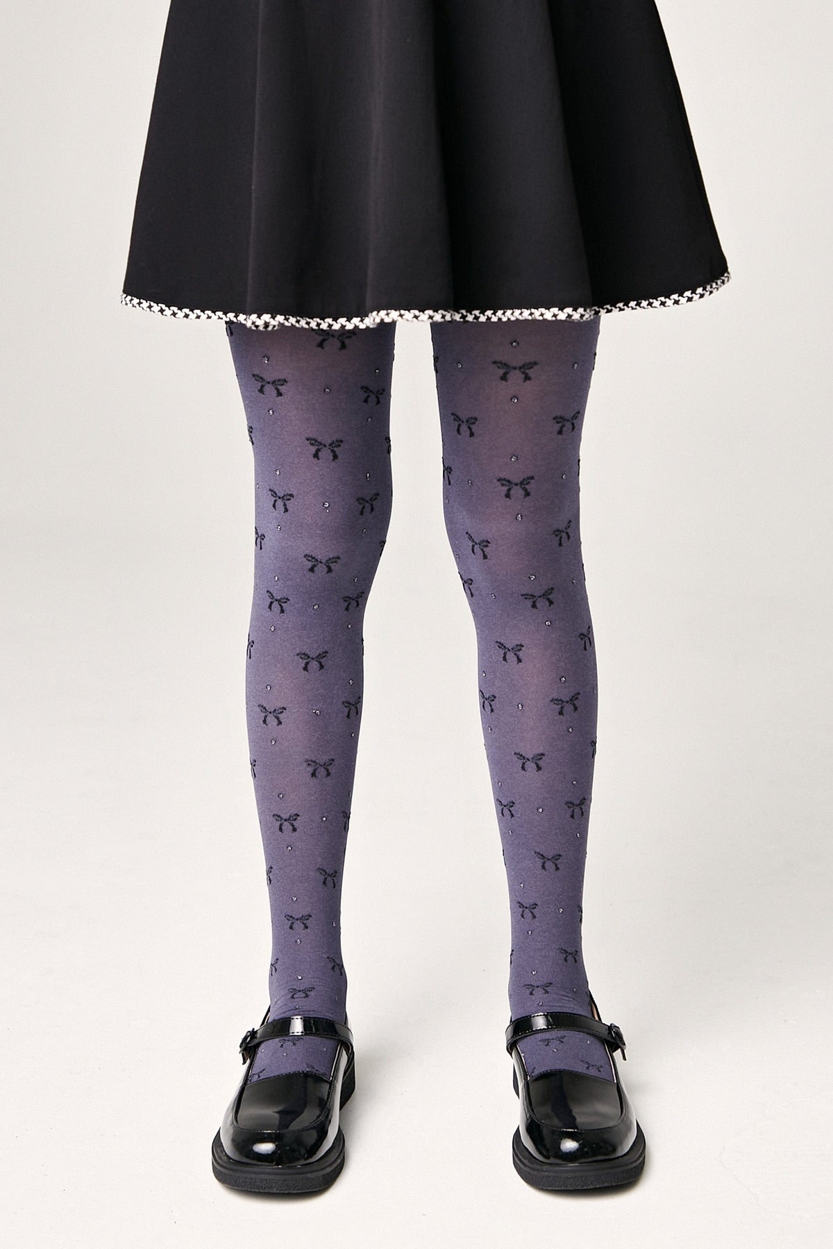 Grey tights featuring a repeating pattern of small black bows and sparkling rhinestones worn with a black skirt and black mary jane shoes.
