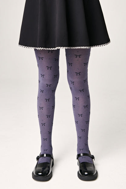 Grey tights featuring a repeating pattern of small black bows and sparkling rhinestones worn with a black skirt and black mary jane shoes.