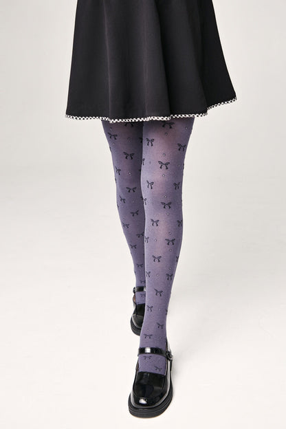 A person wears grey tights patterned with black bows and small sparkles, paired with a short black skirt and black mary jane shoes.