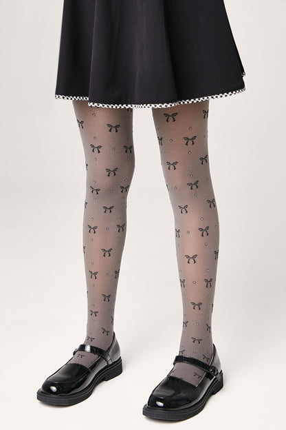 Sheer grey tights patterned with small black bows and subtle glitter accents are worn with a black skirt and shiny black Mary Jane shoes.