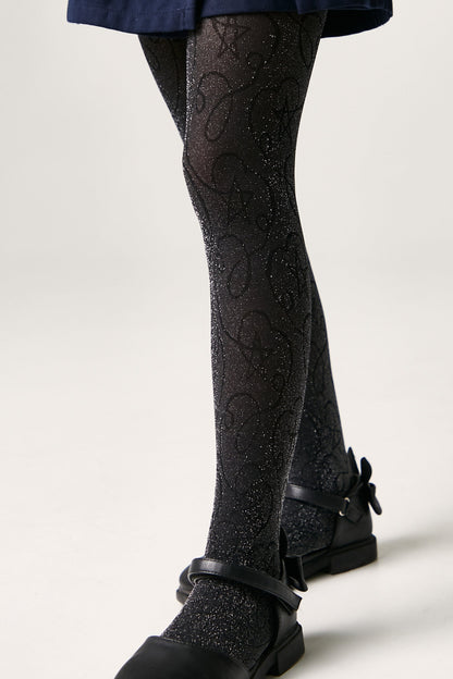 A pair of black glittery tights featuring a subtle swirling pattern and star detail, worn with black strapped flats against a plain white background.