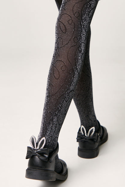 Black glittery tights with a swirling line pattern worn with black shoes featuring a bow and crystal-embellished rabbit ears on the heel.