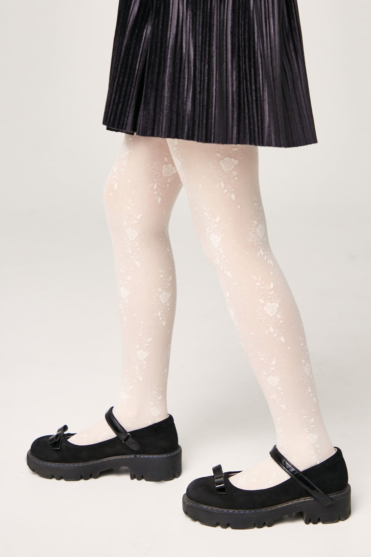 White tights featuring a delicate floral lace pattern worn with a black pleated skirt and black platform mary jane shoes.