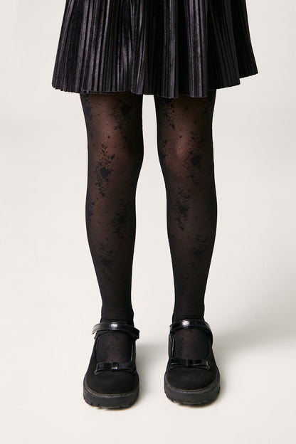 Black patterned tights worn with a black pleated skirt and black patent leather mary jane shoes.