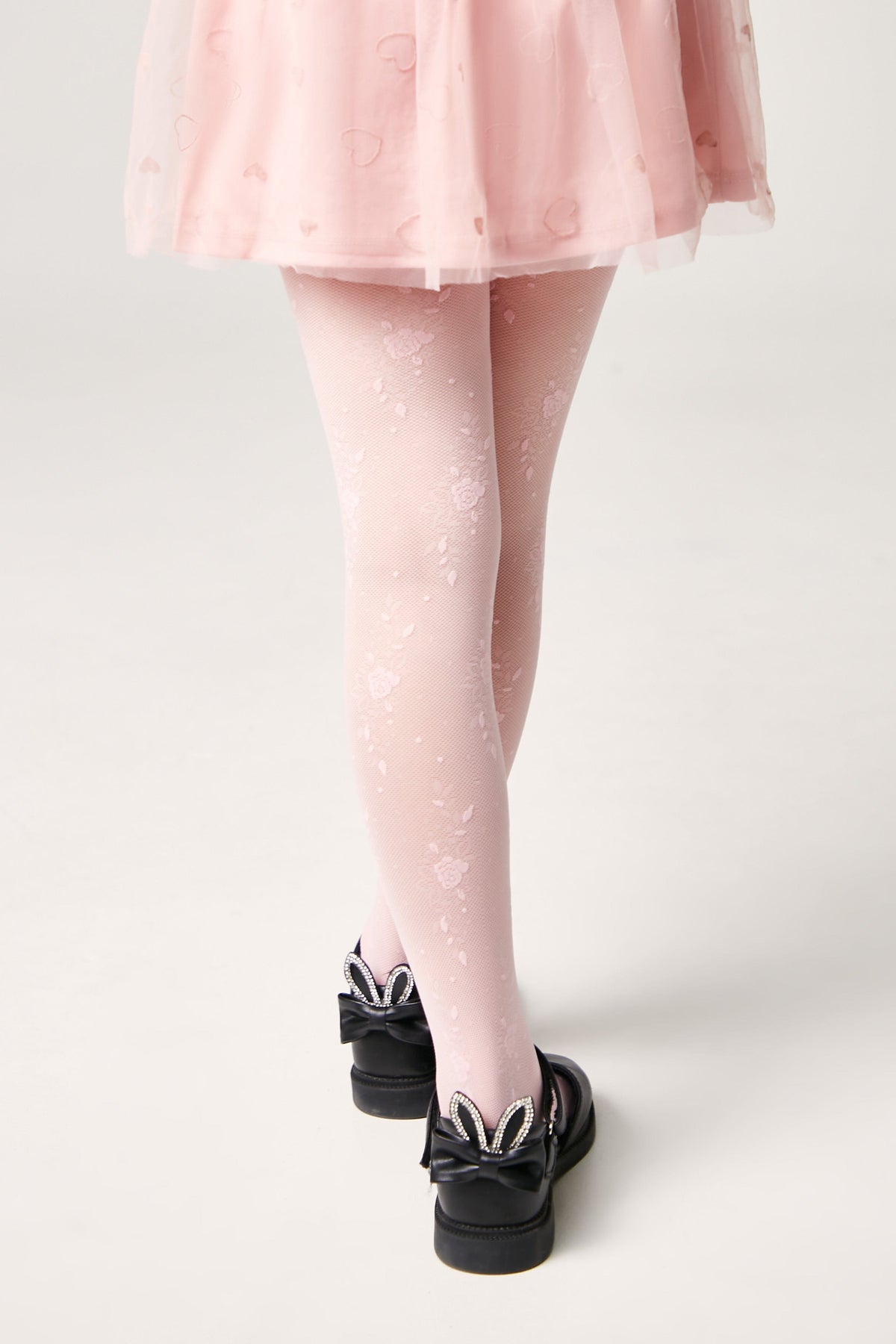 Light pink floral pattern tights worn under a light pink skirt, paired with black shoes featuring bunny-ear bows on the heels.