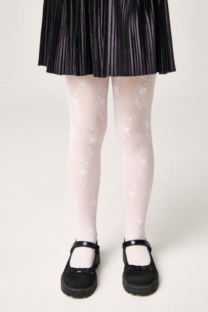 A pair of white floral patterned tights worn with a black pleated skirt and black Mary Jane shoes against a plain white background.